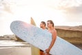 Young couple of happy surfers standing on the beach holding surfboards preparing to surf on high waves during a magnificent sunset Royalty Free Stock Photo