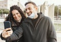 Young couple have fun taking a selfie with smart phone - Friends smile and take a picture wearing protective mask - new normal Royalty Free Stock Photo