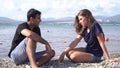 Young couple having an argument by the sea. Action. Man and woman sitting on a stony sea shore, woman feeling ashamed Royalty Free Stock Photo