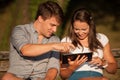 Young couple having fun on a bench in park while socializing over web Royalty Free Stock Photo