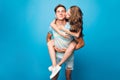 Young couple having fun on blue background in studio. Pretty girl with long curly hair is riding on back of handsome guy Royalty Free Stock Photo