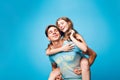 Young couple having fun on blue background in studio. Pretty girl with long curly hair is riding on back of handsome guy Royalty Free Stock Photo