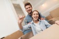 Young couple having fun while moving to new apartment. Moving newlyweds. Girl is sitting in a box. Royalty Free Stock Photo