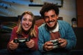 Young couple having fun plaing video games with a console together sitting at couch at home. Two happy friends smiling