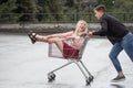 Young couple having fun on shopping trolley. Happy man pushing shopping cart with his girfriend inside Royalty Free Stock Photo