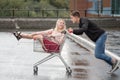 Young couple having fun on shopping trolley. Happy man pushing shopping cart with his girfriend inside Royalty Free Stock Photo