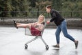 Young couple having fun on shopping trolley. Happy man pushing shopping cart with his girfriend inside Royalty Free Stock Photo