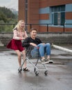 Young couple having fun on shopping trolley. Happy woman pushing shopping cart with her boyfriend inside Royalty Free Stock Photo