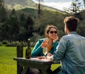 Young couple having lunch on picnic table in countryside with mountains landscape behind Royalty Free Stock Photo