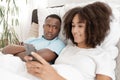 Young couple having problem. Jealous husband is watching his wife use mobile phone on bed at home