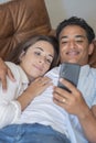 Young couple having relax together using mobile phone laying on the sofa in indoor relaxation leisure activity together. Black boy Royalty Free Stock Photo