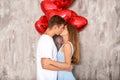 Young couple with heart shaped red balloons kissing near grey wall Royalty Free Stock Photo