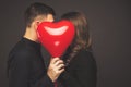 Young couple with heart shaped red balloons near grey wall