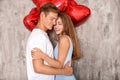 Young couple with heart shaped red balloons near grey wall Royalty Free Stock Photo