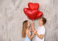 Young couple with heart shaped red balloons near grey wall Royalty Free Stock Photo