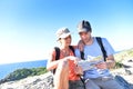 Young couple of hikers looking at map sitting on a rock by the sea