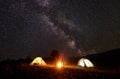 Young couple hikers resting near illuminated tent, camping in mountains at night under starry sky Royalty Free Stock Photo