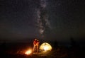 Young couple hikers resting near illuminated tent, camping in mountains at night under starry sky Royalty Free Stock Photo