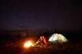 Young couple hikers resting near illuminated tent, camping in mountains at night under starry sky Royalty Free Stock Photo