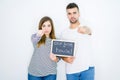 Young couple holding blackboard with our first home text over white isolated background pointing with finger to the camera and to Royalty Free Stock Photo