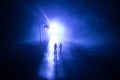 Young couple holding each other hands. Slowly walking under white street lights in night. Dark time. Peaceful atmosphere in mist. Royalty Free Stock Photo