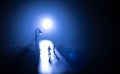 Young couple holding each other hands. Slowly walking under white street lights in night. Dark time. Peaceful atmosphere in mist. Royalty Free Stock Photo