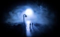 Young couple holding each other hands. Slowly walking under white street lights in night. Dark time. Peaceful atmosphere in mist. Royalty Free Stock Photo