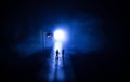 Young couple holding each other hands. Slowly walking under white street lights in night. Dark time. Peaceful atmosphere in mist. Royalty Free Stock Photo