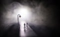 Young couple holding each other hands. Slowly walking under white street lights in night. Dark time. Peaceful atmosphere in mist. Royalty Free Stock Photo