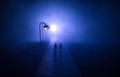 Young couple holding each other hands. Slowly walking under white street lights in night. Dark time. Peaceful atmosphere in mist. Royalty Free Stock Photo