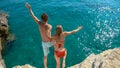 Young couple holding hands jumps off a cliff and into the refreshing cold ocean.