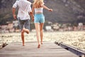 Young couple holding hands running toward water on pier. Summertime holiday. Fun, togetherness, travel concept