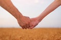 Young couple holds each other`s hands. Field of ripe wheat and the sky on background