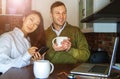 Young couple at home near the laptop are drinking coffee and laughing. Happy international couple make online purchase. Royalty Free Stock Photo