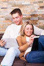 Young couple at home, reading a book and with a tablet Royalty Free Stock Photo