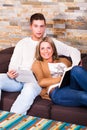 Young couple at home, reading a book and with a tablet, smiling Royalty Free Stock Photo