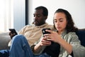 Young Couple At Home Sitting On Sofa Checking Social Media On Mobile Phone Ignoring Each Other Royalty Free Stock Photo