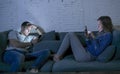 Young couple at home sofa couch smiling happy together but separated ignoring each other concentrated on mobile phone in internet Royalty Free Stock Photo