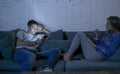 Young couple at home sofa couch smiling happy together but separated ignoring each other concentrated on mobile phone in internet