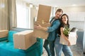 Young couple husband and wife looking happy standing with boxes in their hands leaning towards each other in new appartment moving