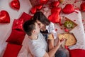 Young couple in intimate moment on bed kissing near red heart balloons. Man and woman enjoying pizza Royalty Free Stock Photo