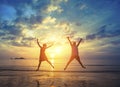 Young couple jumping on the sea beach during amazing sunset.