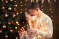 Young couple kissing in christmas lights and decoration, dressed in white, fir tree on dark wooden background, romantic evening, w