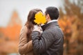 Young couple kissing, hiding faces with autumn yellow maple leave. Royalty Free Stock Photo