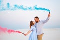 Young couple kissing and holding colored smoke in hands, romantic couple with blue color and red color smoke bomb on beach Royalty Free Stock Photo