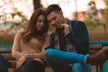 Young couple listening to music, smiling, looking at the phone and sitting on a bench in park Royalty Free Stock Photo