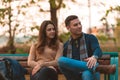 Young couple listening to music, smiling, looking at the phone and sitting on a bench in park Royalty Free Stock Photo