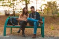 Young couple listening to music,smiling,looking at the phone and sitting on a bench in park Royalty Free Stock Photo