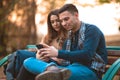 Young couple listening to music,smiling,looking at the phone and sitting on a bench in park Royalty Free Stock Photo