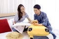 Young couple looking at the directions by phone and map while sitting together on bed at hotel room. Royalty Free Stock Photo